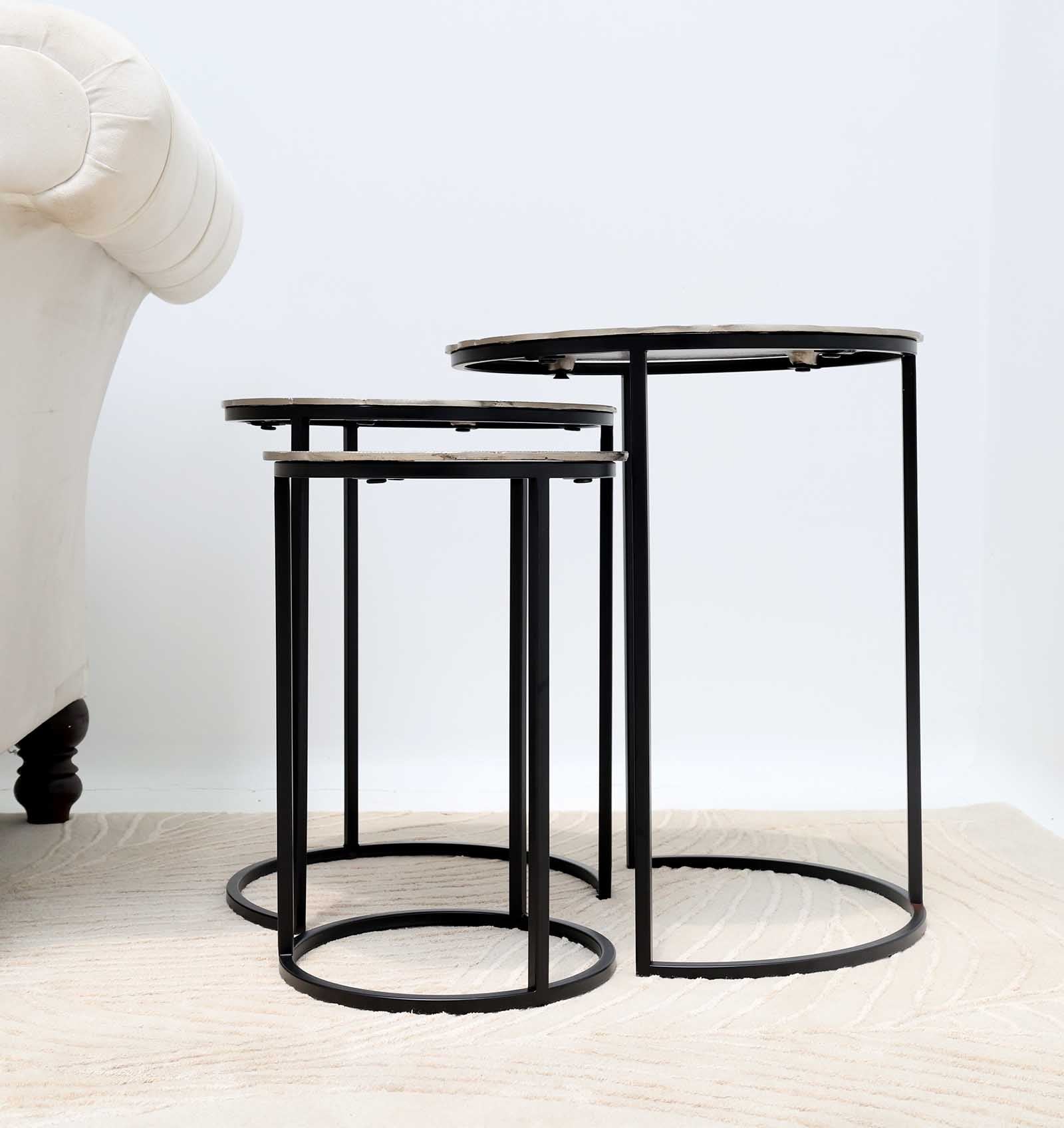 A nesting accent tables featuring antique brass surfaces and sleek iron legs.
