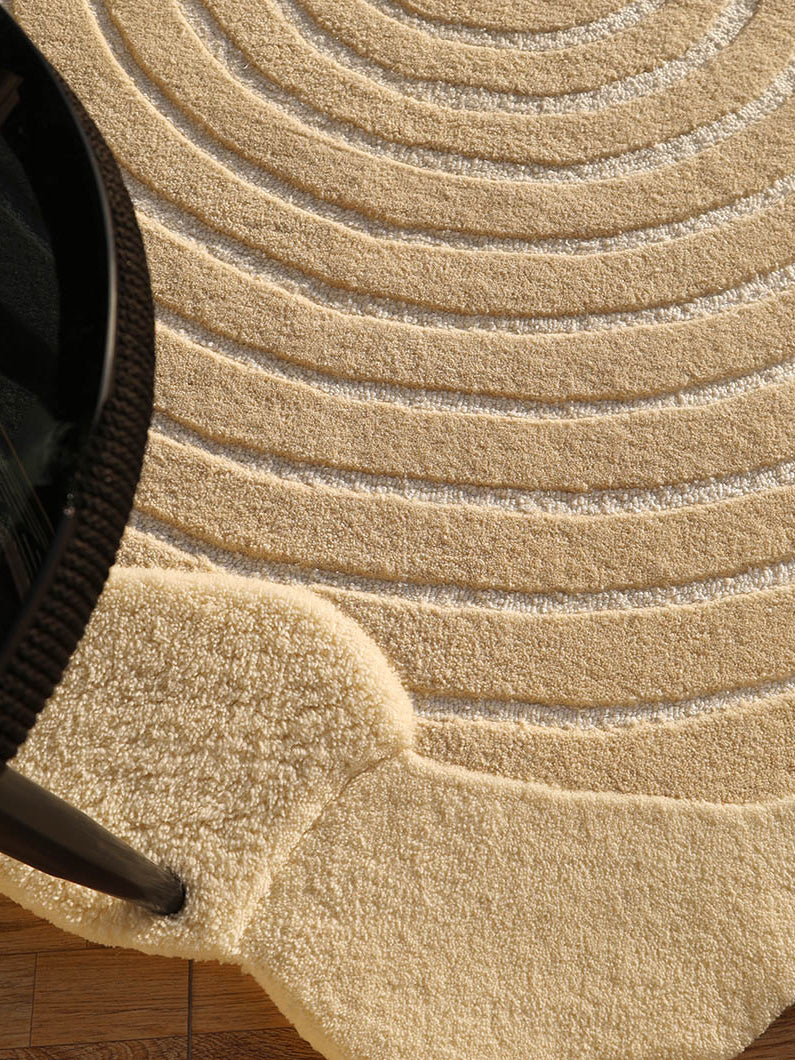 Close-up detailing the luxurious texture underfoot of the beige-colored shaped round handmade rug.