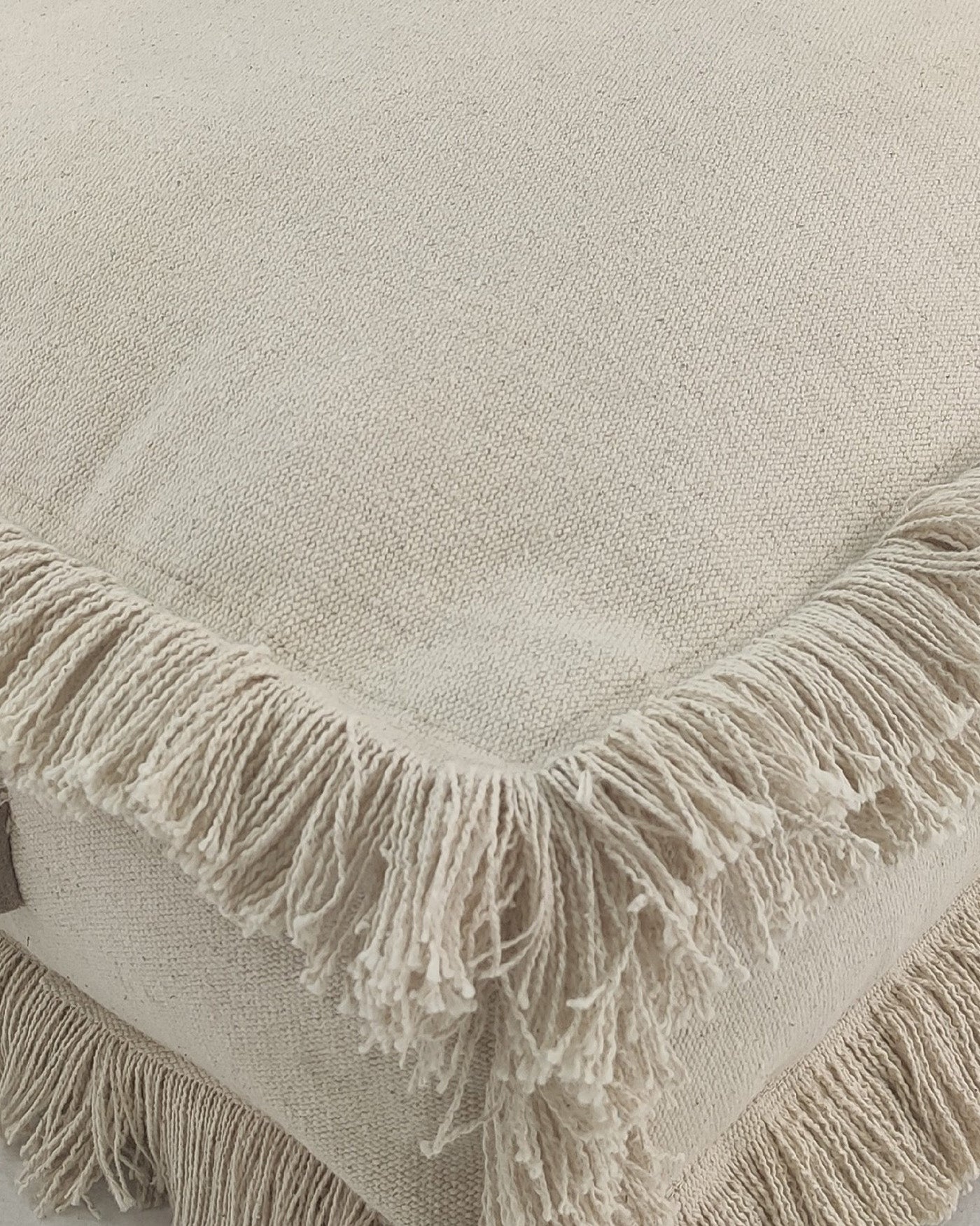 Close-up view of light beige cotton pouf showing its fine woven texture and neatly stitched leather handle.