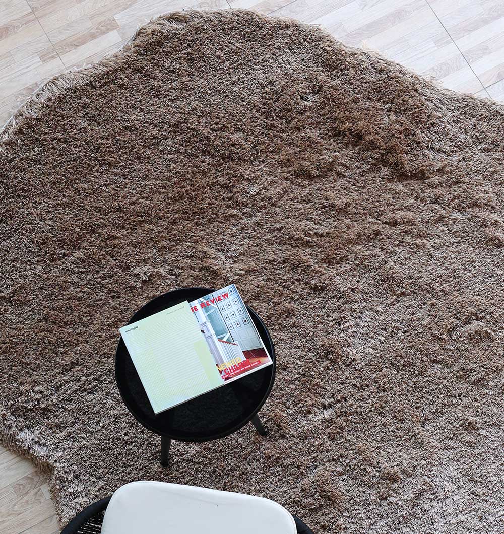 Top close-up of the irregular brown shaggy rug, detailing the plush texture and modern design from an overhead view.