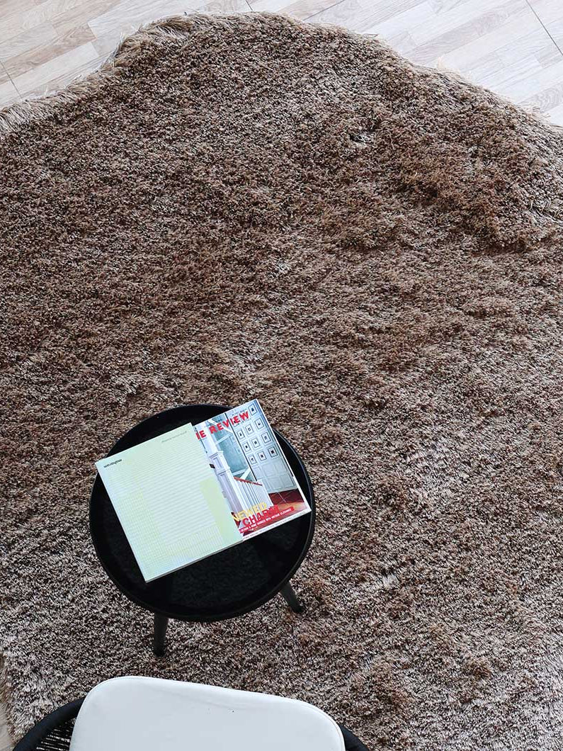 Top close-up of the irregular brown shaggy rug, detailing the plush texture and modern design from an overhead view.